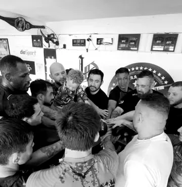 Atletas e professores em roda, com as mãos juntas no centro, antes do treino.
